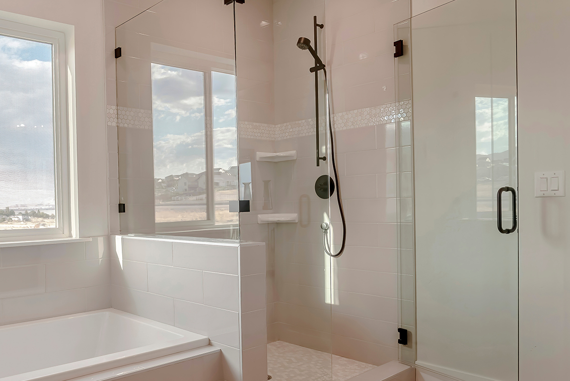 Built in bathtub with black faucet and shower stall with half glass enclosure. Interior of bathroom with view of snowy landscape and cloudy sky through the window.